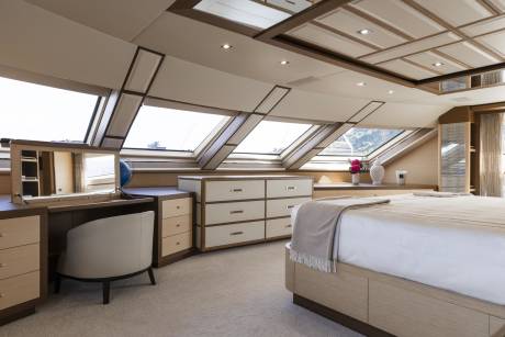 A luxurious bedroom features a vanity, dresser, and bed beneath angled skylights offering a glimpse of the outdoors.