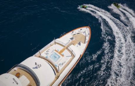 Two jet skiers create white wakes as they race through the deep blue ocean alongside a luxurious yacht.