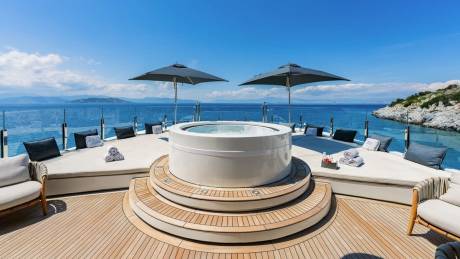 Luxurious yacht deck with a circular jacuzzi, plush loungers, and umbrellas offers a perfect oasis against a stunning ocean backdrop.
