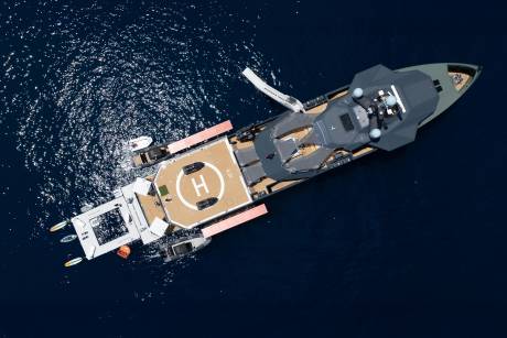 A luxurious superyacht with a helipad and tenders rests on the sparkling blue ocean.