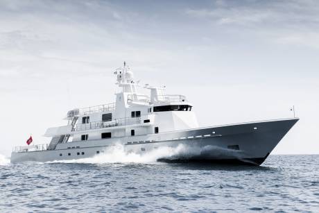 A sleek white yacht cuts through the choppy blue sea, leaving a powerful wake under a pale, cloudy sky.