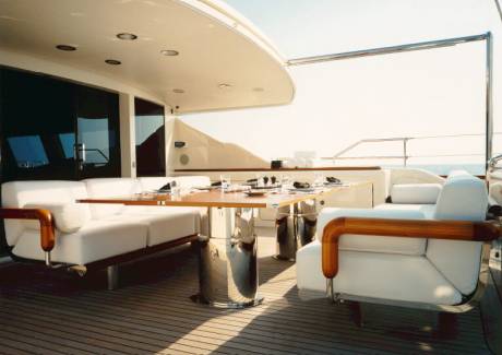 A beautifully set dining table awaits on the deck of a luxurious yacht, surrounded by comfortable white seating.