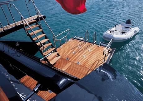 A luxurious yacht's teak deck and wooden stairs lead to the turquoise water where a tender awaits.