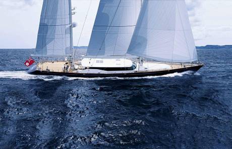 A majestic sailing yacht glides through the deep blue ocean under a cloudy sky.