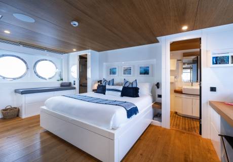 Luxurious yacht cabin features a comfortable bed, porthole windows, and an ensuite bathroom for ultimate relaxation.