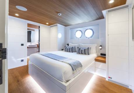 Luxurious yacht cabin features a comfortable bed, porthole windows, and warm wood accents for a serene escape.