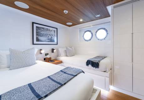 Two beds with nautical-themed linens are neatly made in this bright, modern cabin with porthole windows.