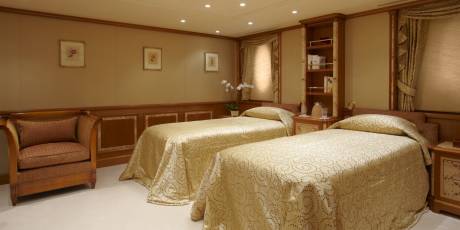 Luxurious twin beds with ornate gold patterned linens await in this elegant stateroom.