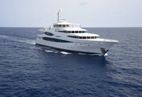A sleek white superyacht glides through the deep blue ocean under a clear sky.