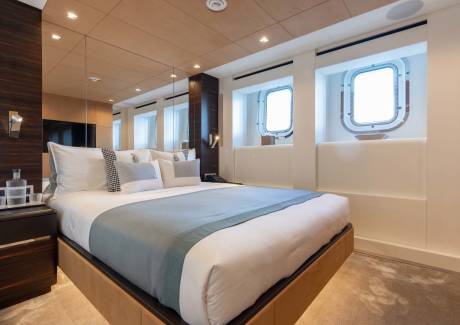 Luxurious yacht stateroom features a king-sized bed, elegant wood paneling, and porthole windows offering ocean views.