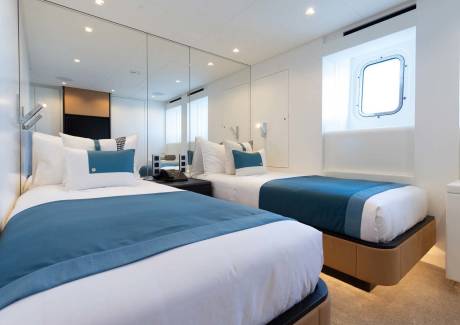 Two twin beds with crisp white linens and teal accents create a serene sleeping space aboard this luxurious yacht.