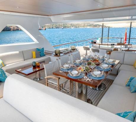 A beautifully set dining table awaits guests on the deck of a luxurious yacht, overlooking the sparkling blue sea.