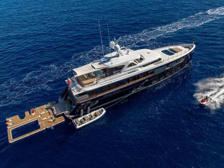 A sleek yacht glides through the deep blue sea, accompanied by a jet ski leaving a foamy wake.