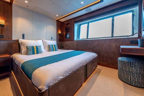 Luxurious yacht cabin features a comfortable bed with decorative pillows and a striking turquoise accent runner.