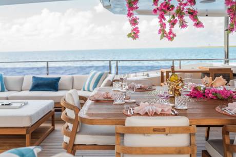A beautifully decorated outdoor dining area overlooking a serene ocean view, with a wooden table set with elegant tableware and surrounded by comfortable seating.
