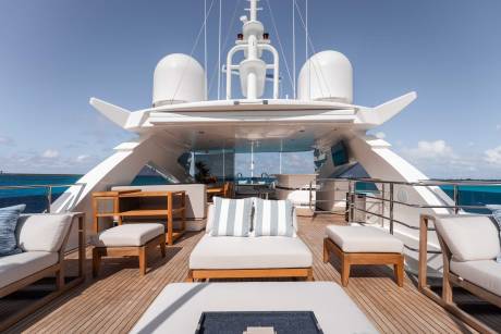 A luxurious yacht with a spacious deck featuring comfortable seating areas, surrounded by a serene blue ocean and clear sky.