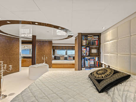 Luxurious yacht bedroom features a plush bed, built-in bookshelves, and stunning ocean views through large windows.