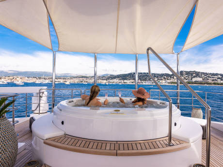 Two women relax in a hot tub on a yacht, enjoying the stunning coastal views and a glass of champagne.