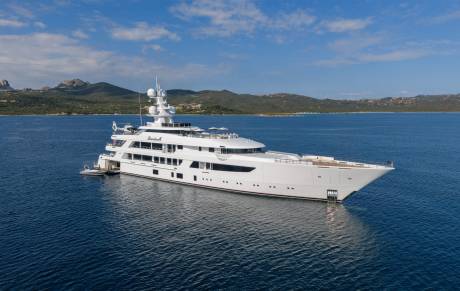 The luxurious Boardwalk superyacht glides serenely across the deep blue waters, with a verdant, hilly coastline in the background.