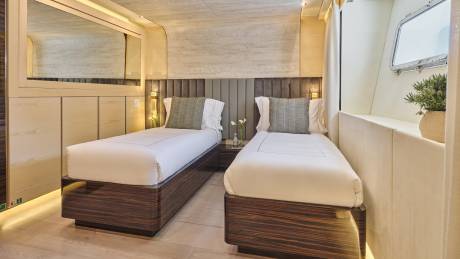 A cozy and modern bedroom with two twin beds, wooden headboards, and decorative lighting, set against a neutral-toned wall.