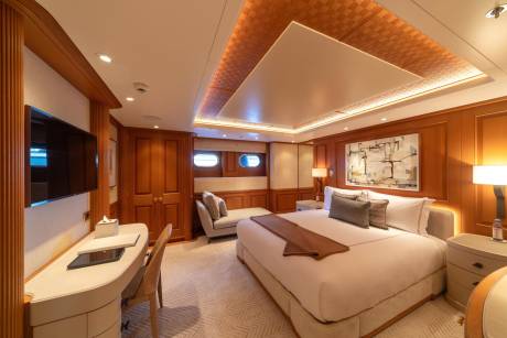 Luxurious yacht accommodations feature a spacious master suite with a comfortable bed, elegant artwork, and a private desk area.