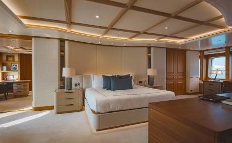 Luxurious yacht accommodations feature a spacious bedroom with elegant wooden accents and a serene view of the sea.