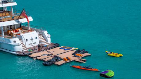 A luxurious yacht is moored next to a floating dock laden with water toys and jet skis.