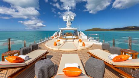 Luxurious sun loungers and a hot tub await guests on the expansive deck of this superyacht, anchored in turquoise waters under a brilliant blue sky.