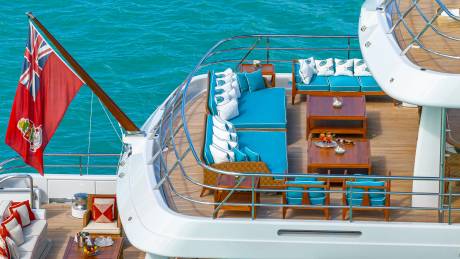 Luxurious yacht seating in vibrant turquoise and white cushions awaits guests on a sun-drenched deck overlooking the sparkling ocean.