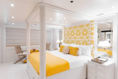 A luxurious yacht cabin features a vibrant yellow and white ikat-patterned headboard and a plush yellow throw on a grand four-poster bed.