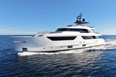 A sleek white yacht glides through the deep blue ocean under a clear sky.