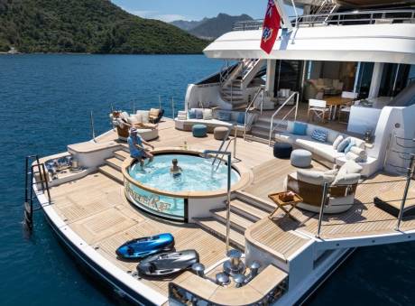 A luxurious yacht offers a refreshing dip in its jacuzzi and ample lounging space amidst a stunning coastal backdrop.