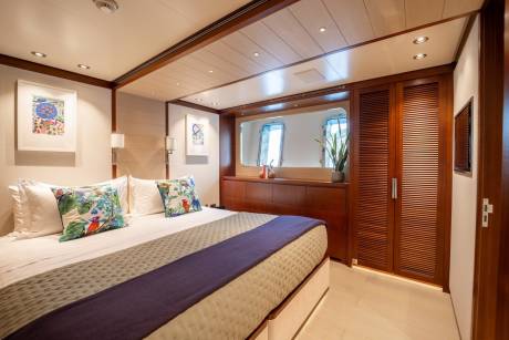 A luxurious yacht cabin features a comfortable bed, elegant artwork, and a large mirror reflecting the serene sea views.