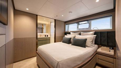A luxurious yacht cabin features a comfortable bed, a sleek en-suite bathroom, and a porthole window offering ocean views.