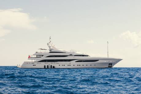 A luxurious white yacht glides across the deep blue ocean under a hazy sky.