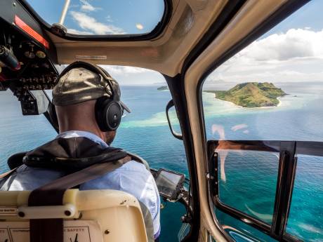 A pilot in a helicopter soars over the turquoise waters and lush green islands of a tropical paradise.