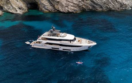 A luxurious yacht anchors in crystal-clear turquoise waters near a rugged cliff face.