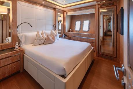 Luxurious yacht accommodations feature a plush bed, elegant wood finishes, and porthole windows offering a glimpse of the sea.
