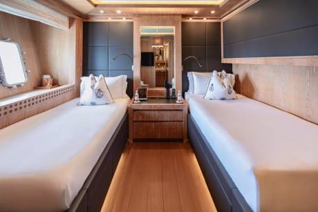Twin beds are neatly made with nautical-themed pillows in this luxurious yacht cabin.