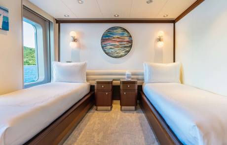 Twin beds dressed in crisp white linens flank a circular abstract artwork in this serene yacht stateroom.