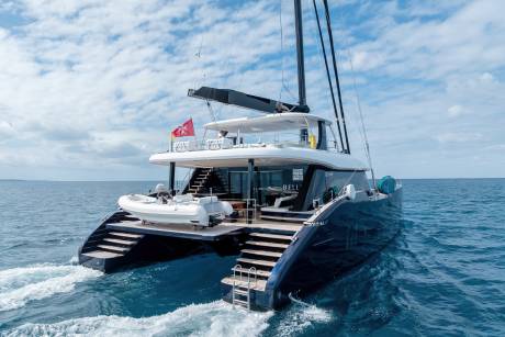 A large, luxurious yacht with multiple decks and a Turkish flag is sailing on the open ocean, surrounded by a clear blue sky with scattered clouds.