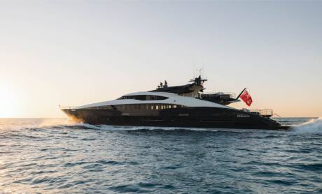 A sleek, dark yacht cuts through the calm, sun-drenched ocean waters.