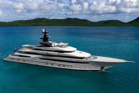 A luxurious superyacht named Whisper glides through the tranquil turquoise waters off a lush, green coastline.
