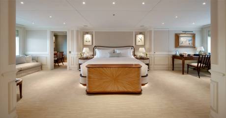 A spacious and elegantly furnished bedroom with a large bed, wooden furniture, and a cozy seating area in the background.