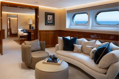 A cozy and luxurious living room with large windows overlooking the ocean, featuring plush seating, wooden paneling, and decorative accents.