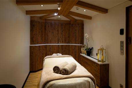 A cozy and inviting massage room with wooden beams, a massage table with towels, and various decorative elements such as candles and an orchid.