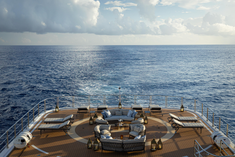 A luxurious yacht deck with comfortable seating arrangements overlooking the vast, serene expanse of the open ocean under a cloudy sky.
