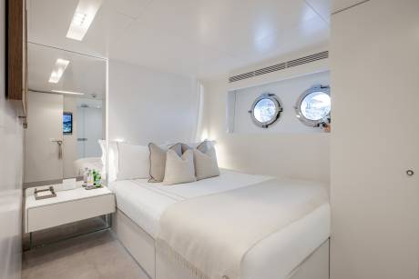 A bright and airy bedroom with a comfortable-looking bed, two circular windows, and a minimalist design aesthetic.