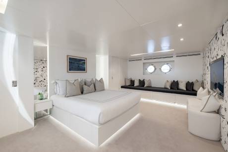 A modern, minimalist bedroom with a large white bed, built-in seating along the walls, and various decorative elements such as artwork and lighting fixtures.