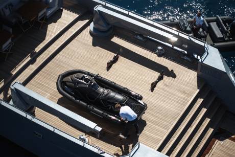 A wooden deck on a boat, with a golf bag and other equipment visible in the foreground, and the open water and sky in the background.